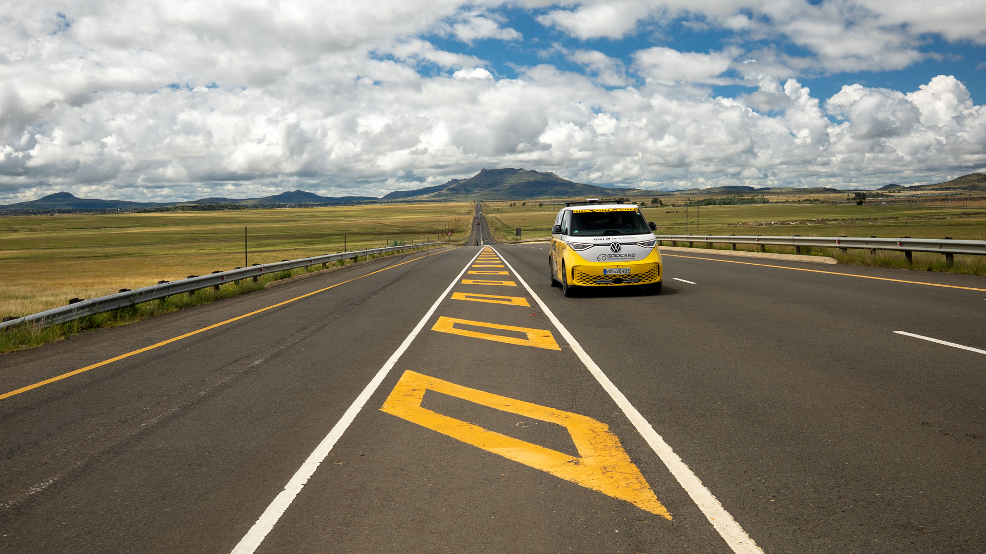 A yellow and white VW ID bus is driving on a country road.