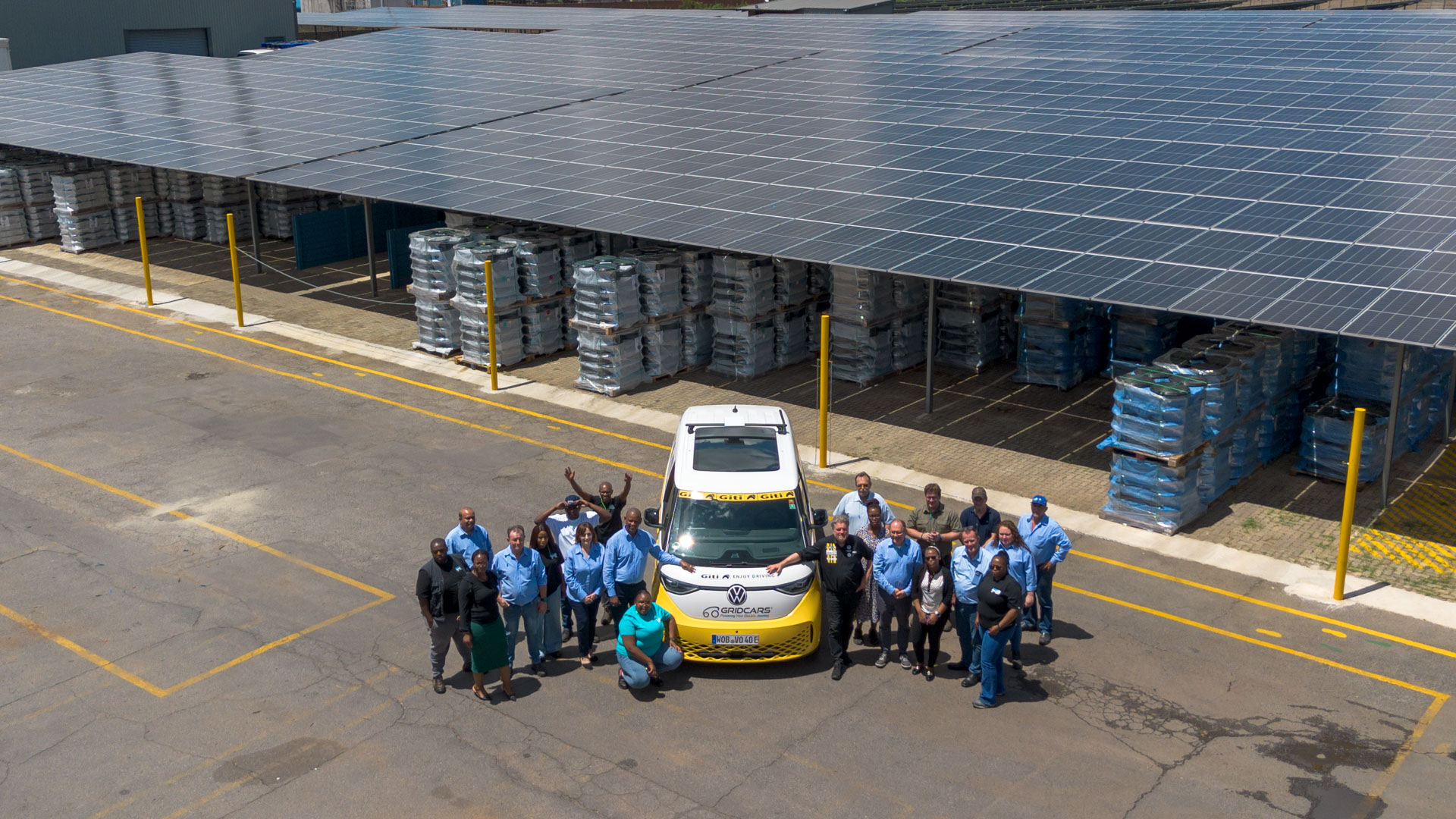 A yellow and white VW ID bus stands next to a group of people who are all looking at the camera and smiling.