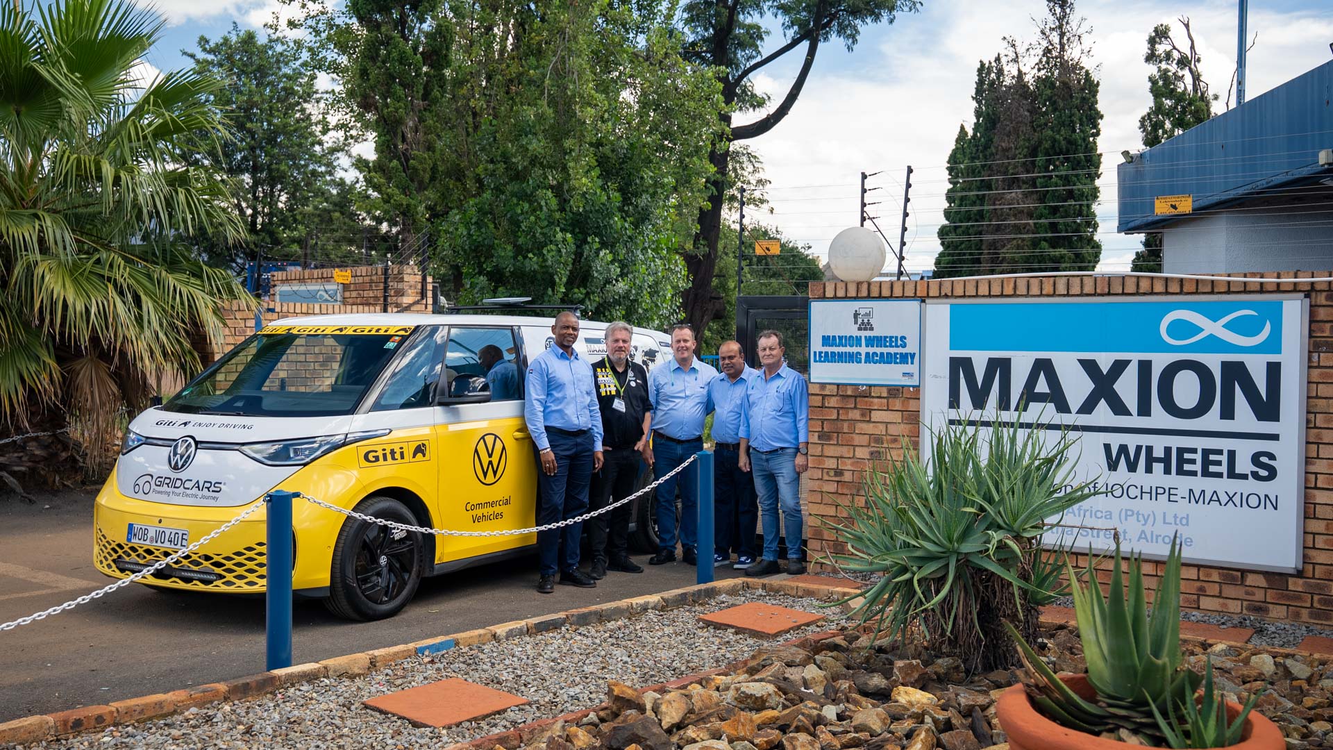 A yellow and white VW ID bus stands next to five people and a sign that says Maxion Wheels.