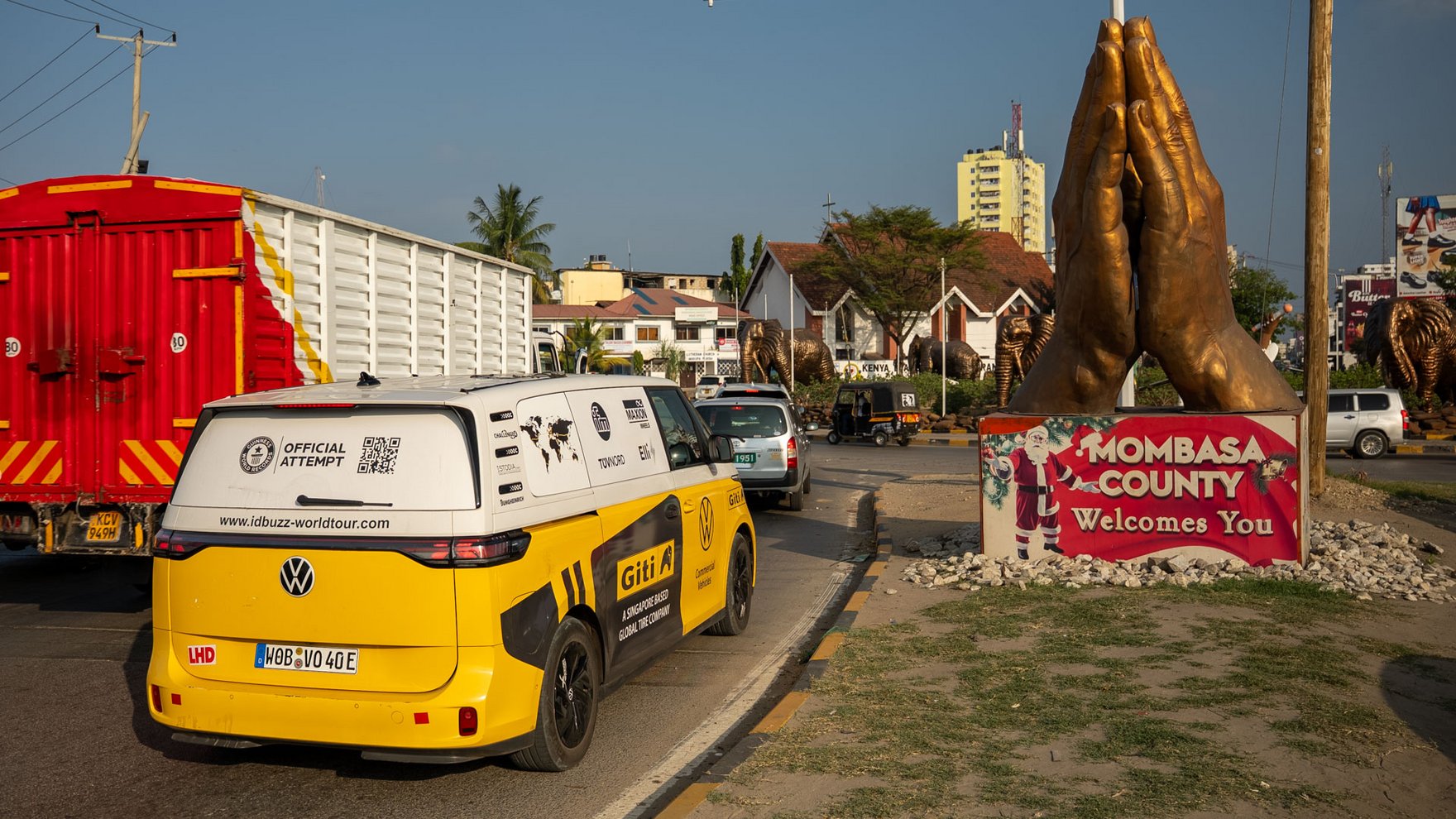A yellow and white VW ID bus is driving in city traffic and a red sign notes that this is Mombasa 