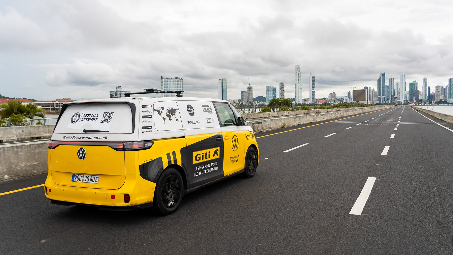 yellow volkswagen van driving on three-lange asphalt highway towards a skyline of a larger city