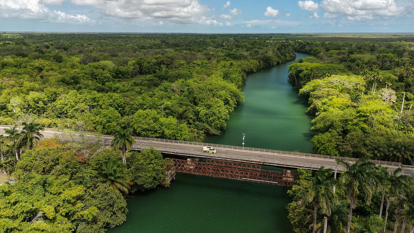 Vast green landscape with green river cutting through the middle and a bridge crossing over the river