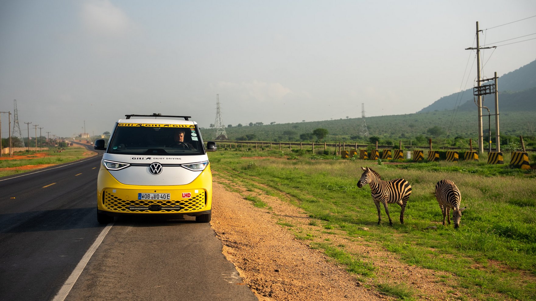 A yellow and white VW ID bus is parked on a side of a road, next to two zebras 
