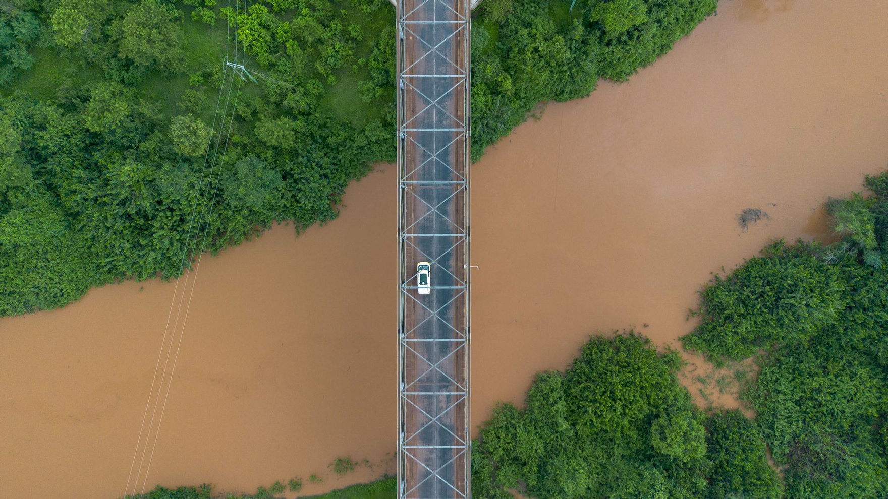 Birds eye view of a vehicle passing a bridge over a brown river
