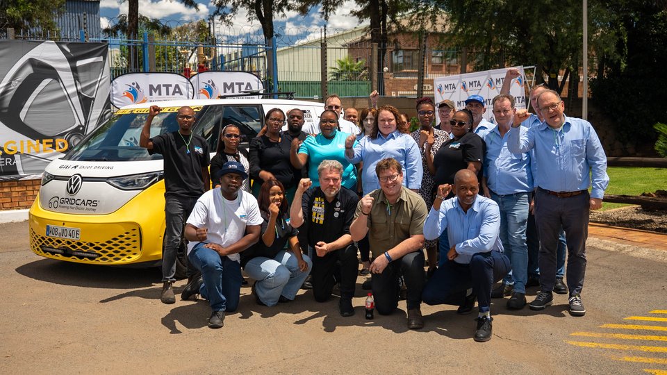 A yellow and white VW ID bus next to a group of Maxion employees who are making a fist and smiling at the camera.